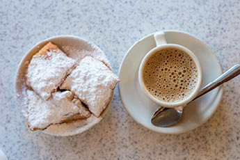 Beignets (French style donuts) topped with sugar and a cup of coffee in the background