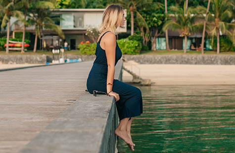 side view of attractive girl sitting in dress on pier near ocean